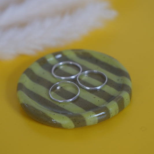 Round ceramic dish with green and brown striped pattern on a yellow background