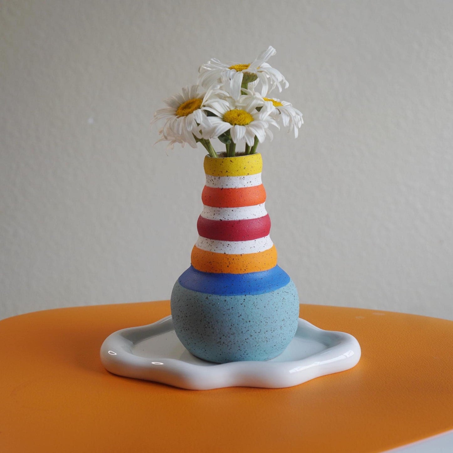 Colorful striped vase with flowers on a white surface