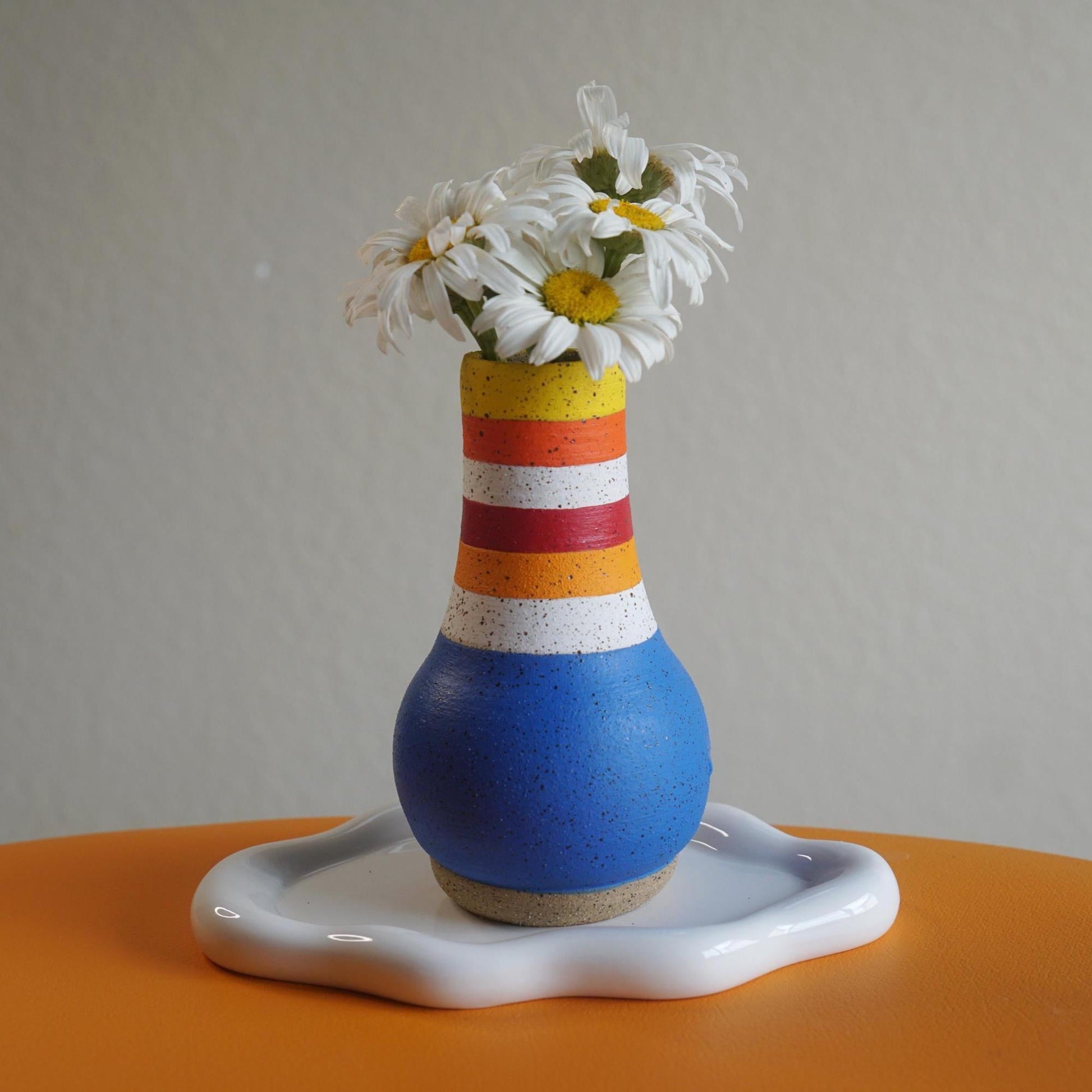 Colorful striped vase with flowers on a white surface