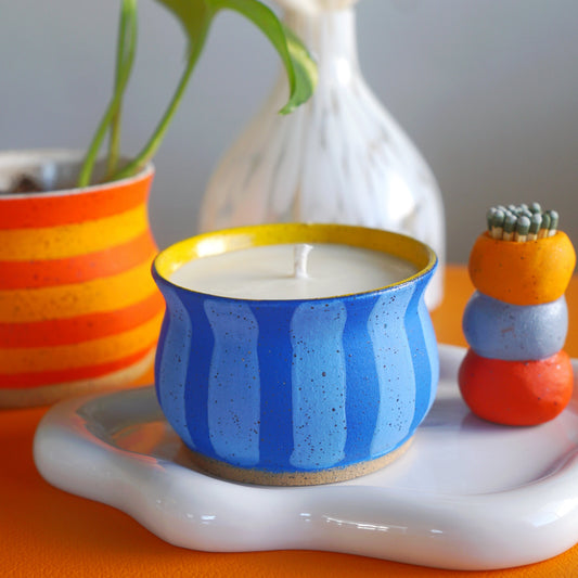 Ceramic candle holder with blue and yellow stripes on a white surface with decorative items.