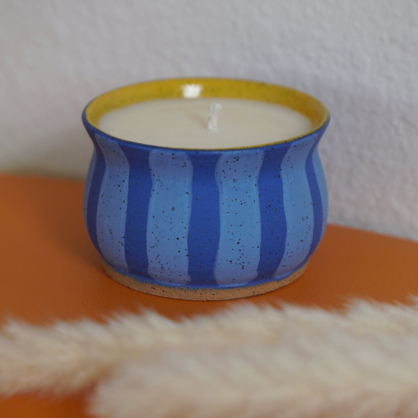 Candle in a blue striped container on a textured surface