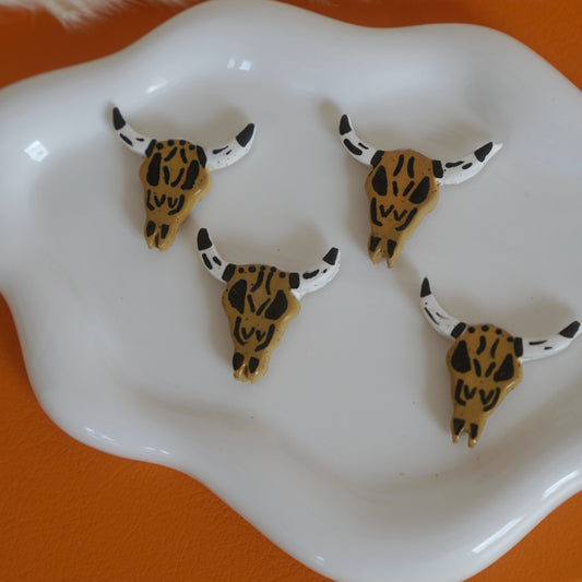 Four small animal skull figurines with decorative horns on a white plate against an orange background.