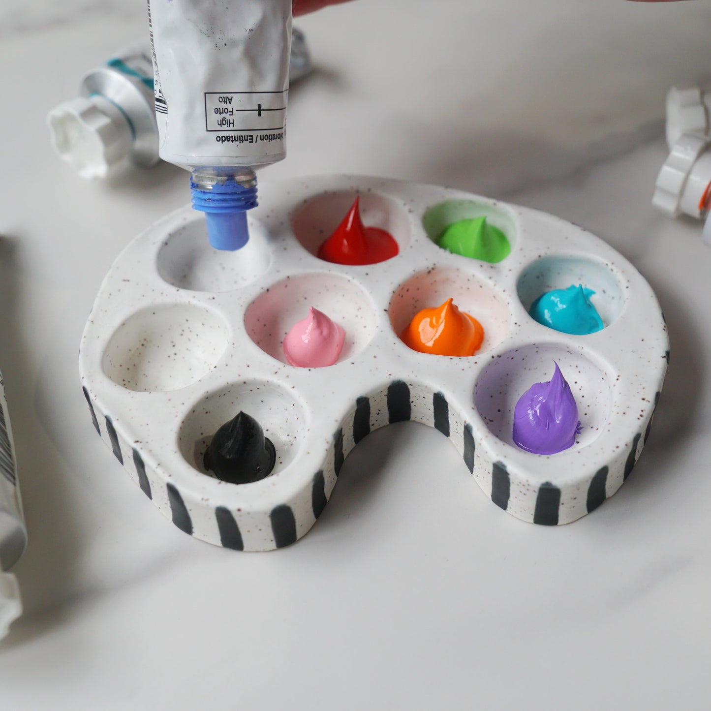 Paint palette with colorful paint and open paint tubes on a white surface