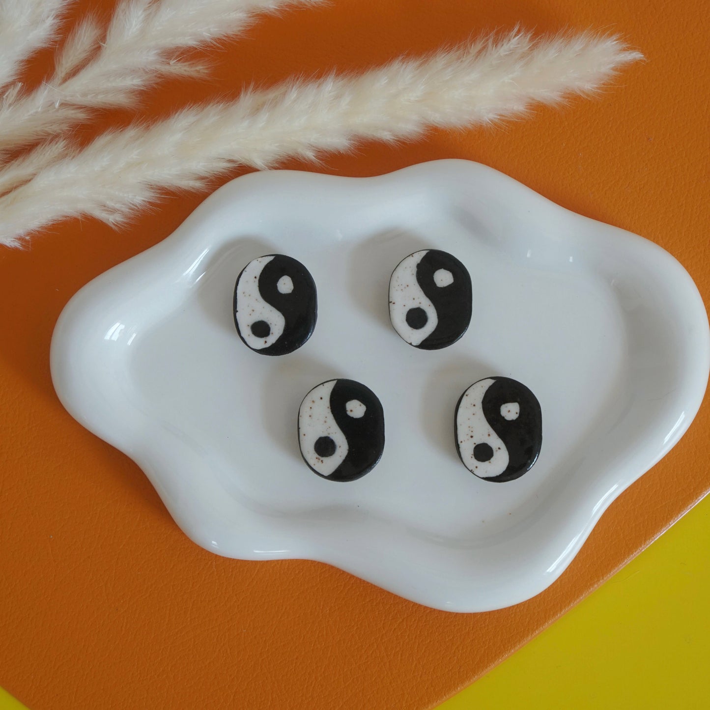 Yin yang magnets on a white dish with dried pampas grass on an orange and yellow background