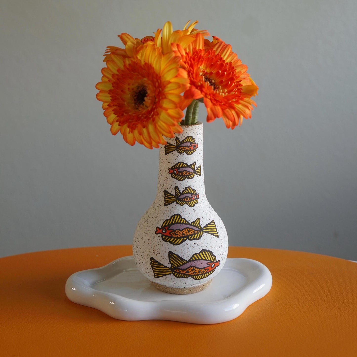 Decorative vase with fish patterns and orange flowers on a gray background