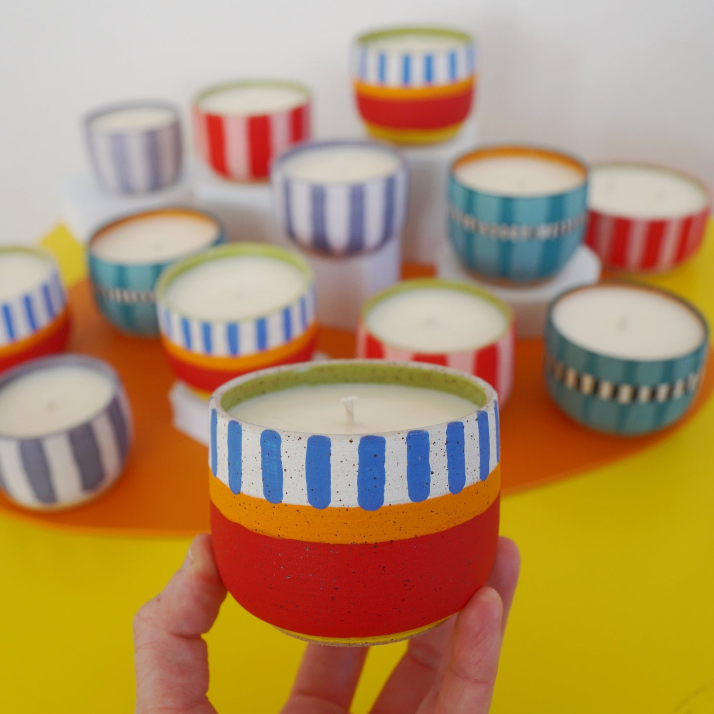 Colorful striped candles on a yellow surface with a hand holding one candle.