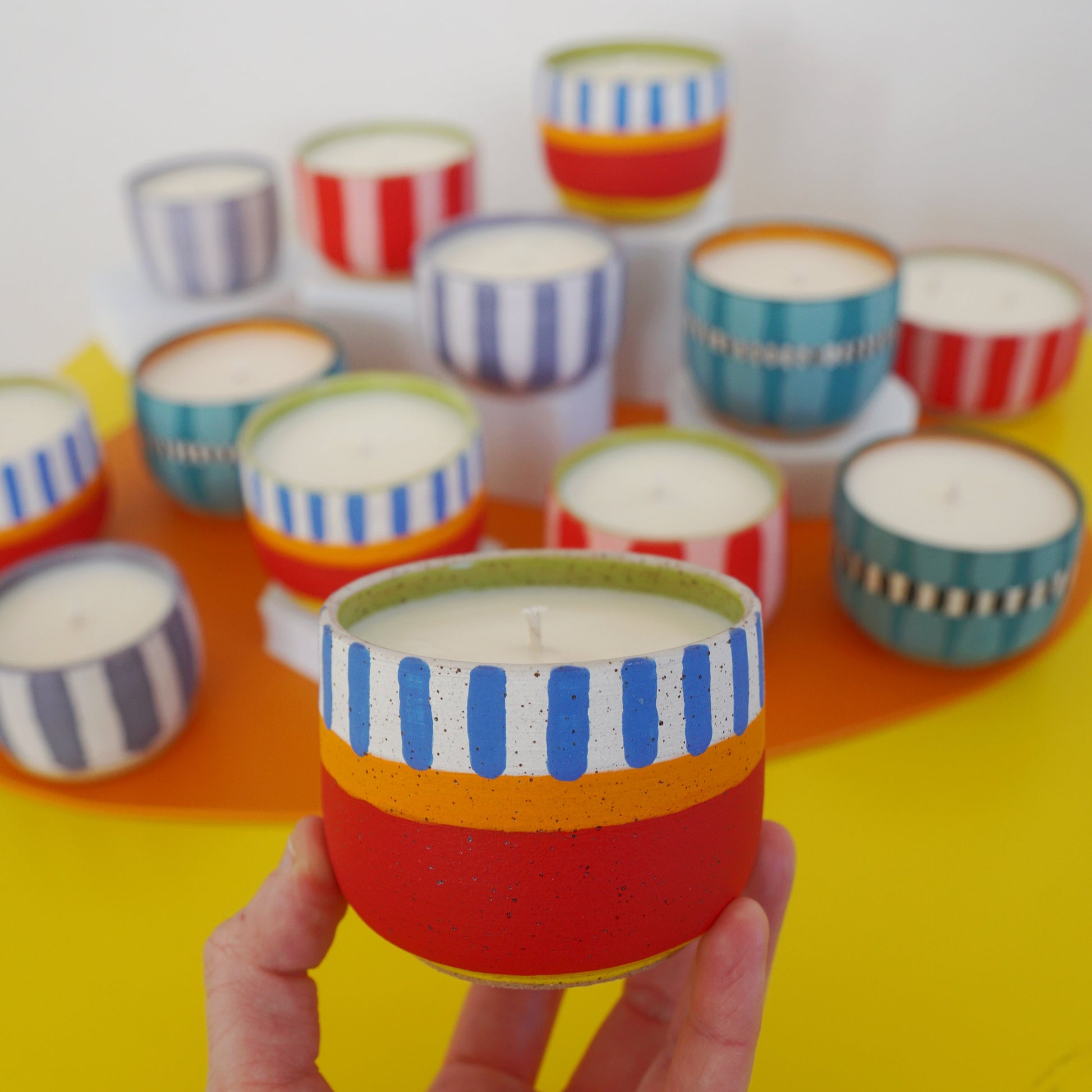 Colorful striped candles on a yellow surface with a hand holding one candle.