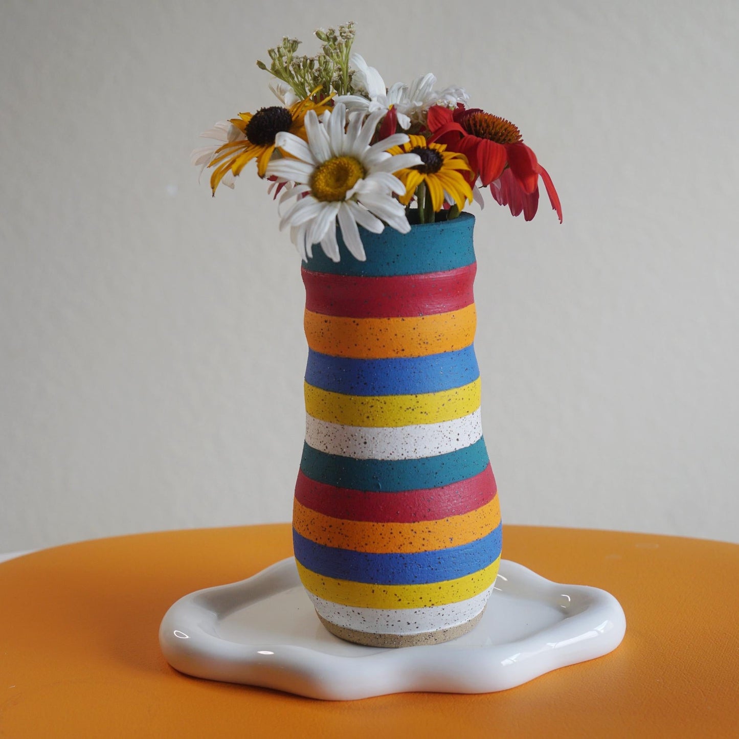 Colorful striped vase with flowers on a white surface