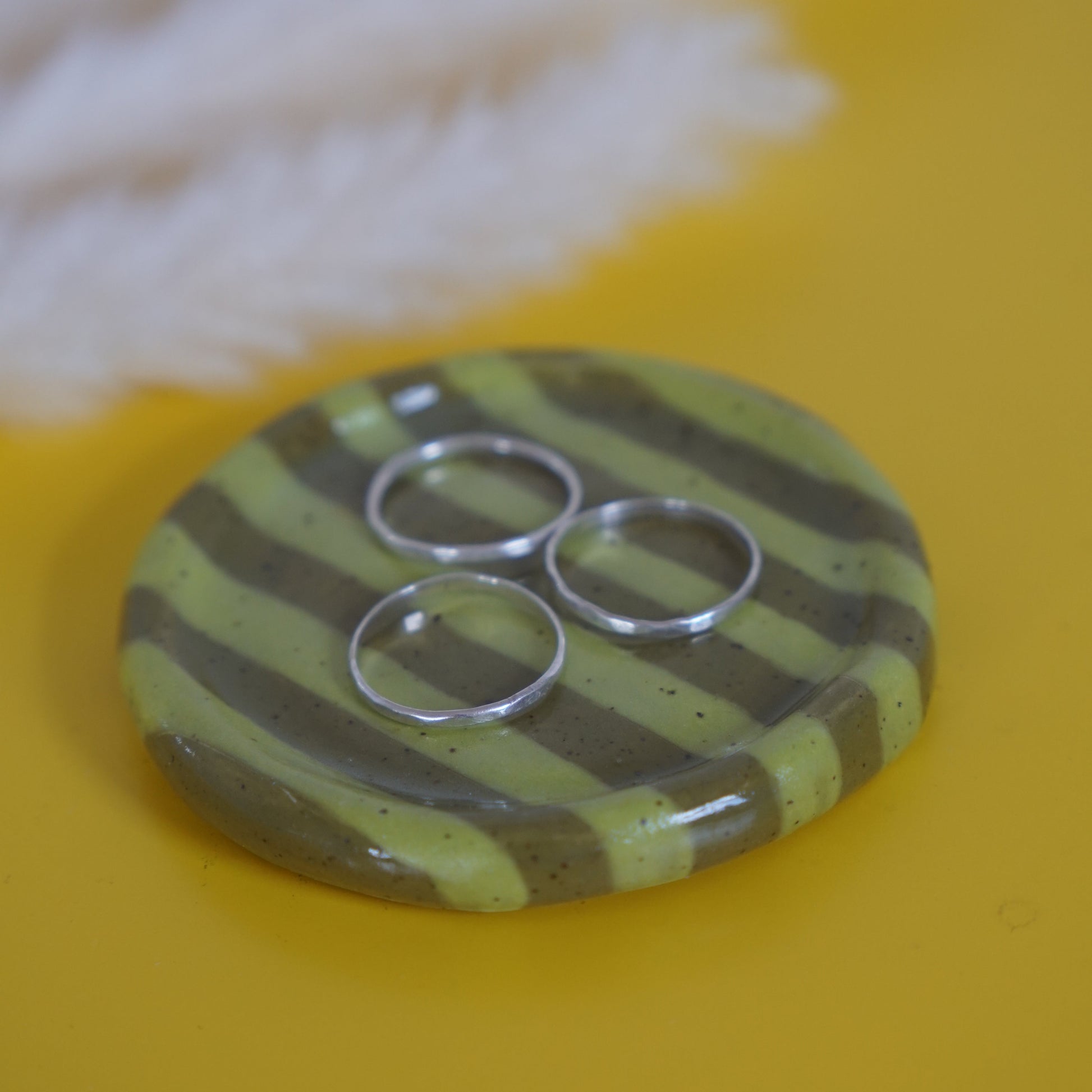 Round ceramic dish with green and brown striped pattern on a yellow background
