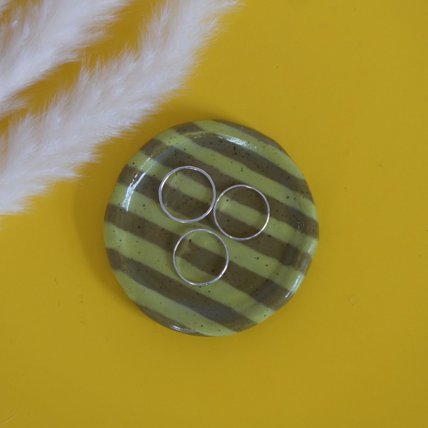 Striped green ceramic ring dish with three circular rings on a yellow background