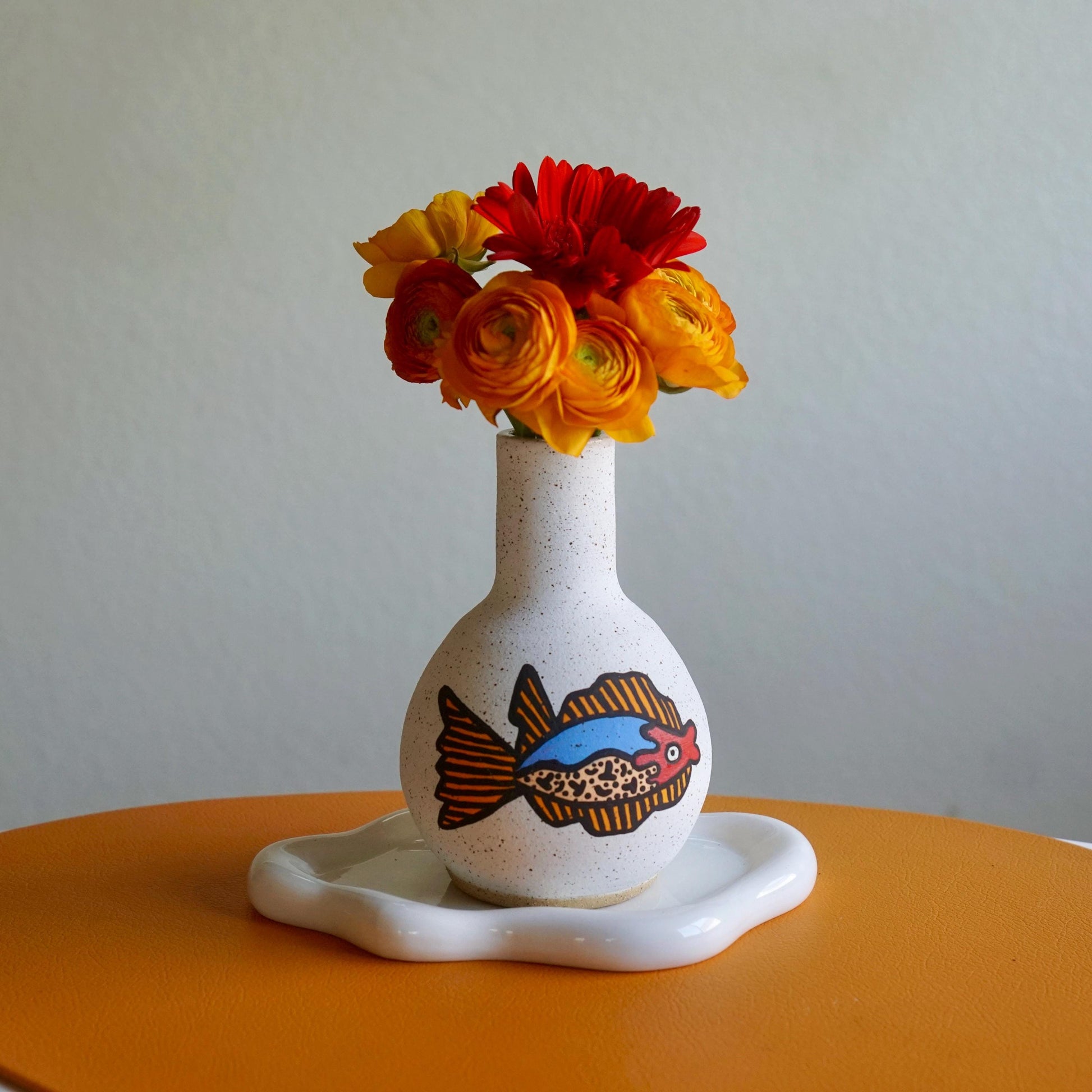 Ceramic vase with fish design and colorful flowers on a white background