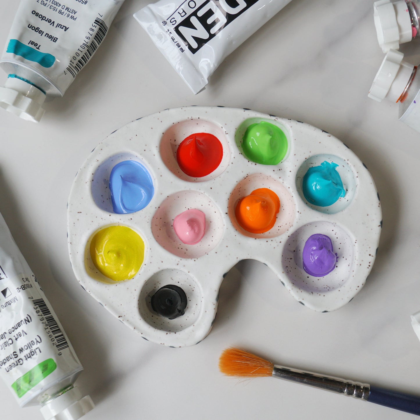 Colorful paint palette with open paint tubes and a brush on a white background