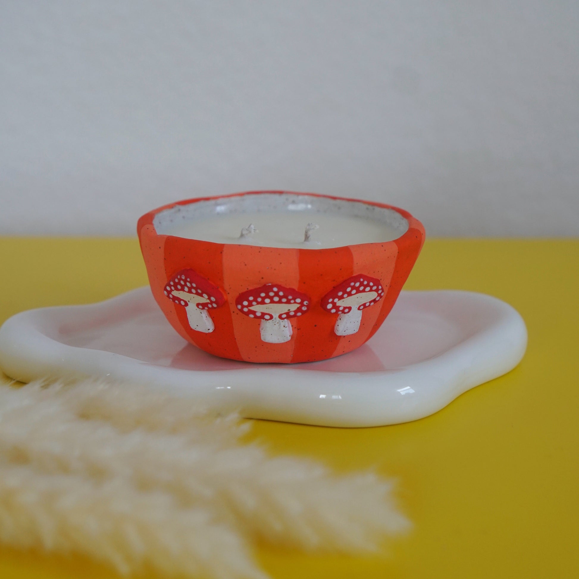 Candle in an orange container with mushroom design on a white plate against a yellow background