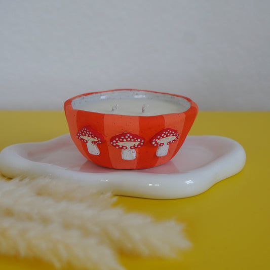 Candle in an orange container with mushroom design on a white plate against a yellow background