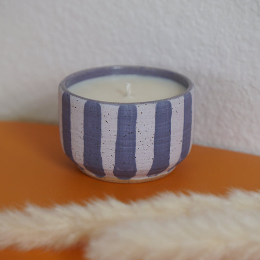 Candle in a striped ceramic holder on an orange surface with a white textured background