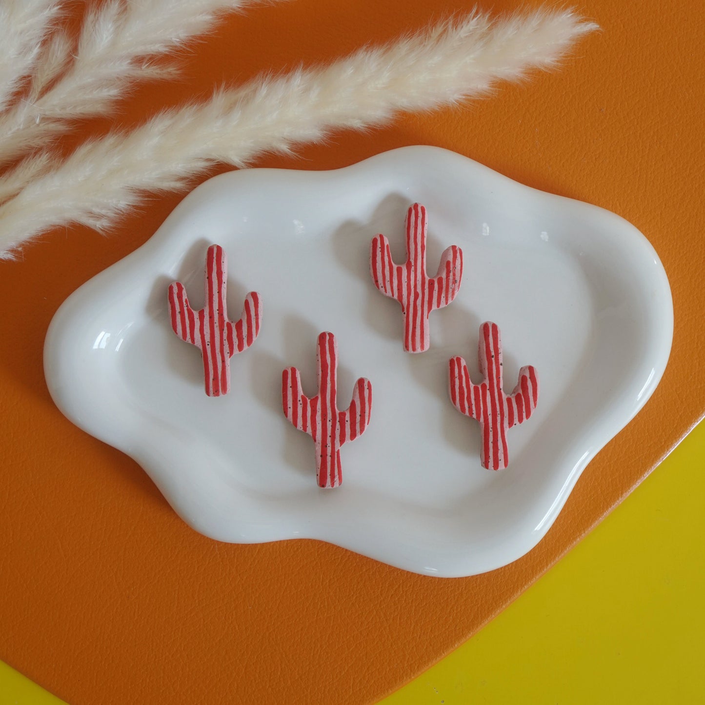 Red cactus-shaped magnets on a white dish with a natural branch on an orange and yellow background