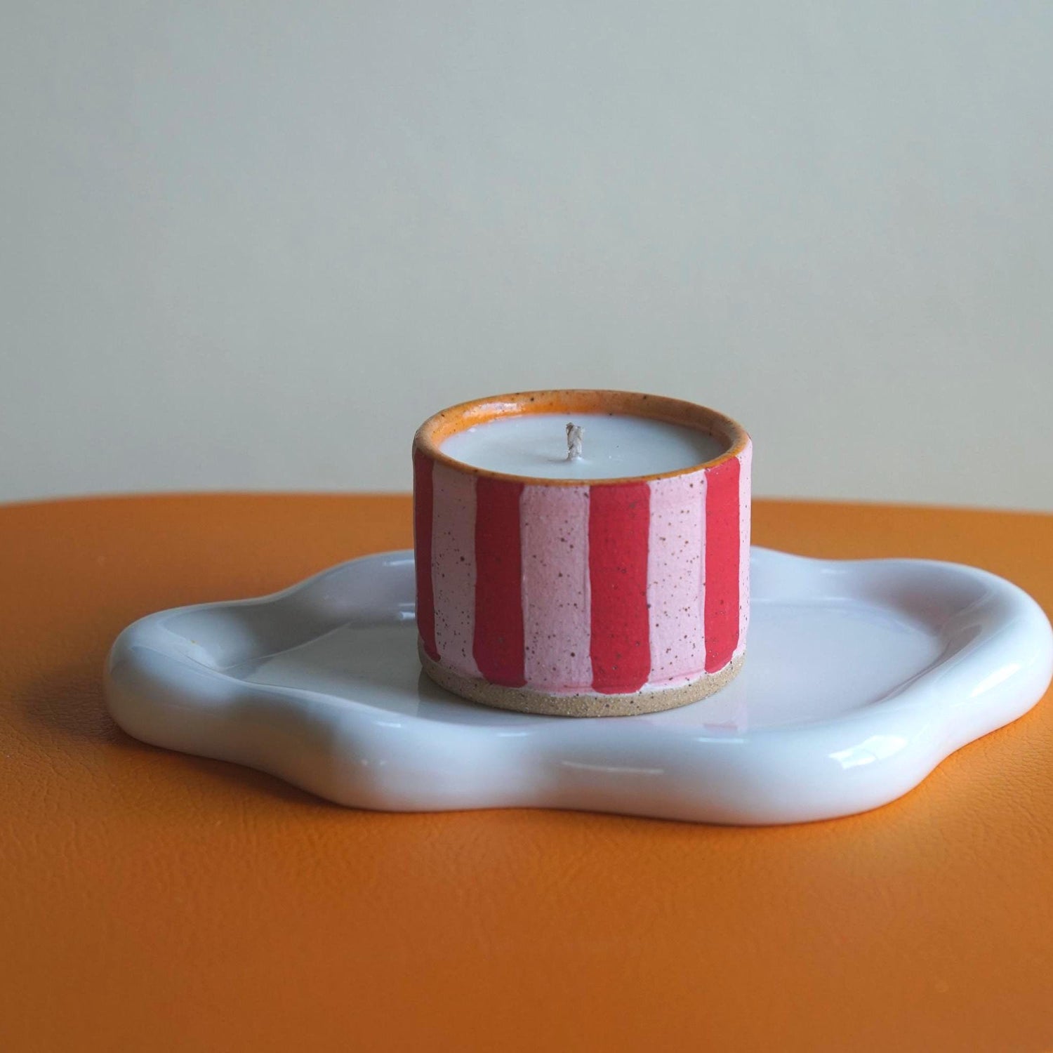 Candle with red and white striped design on a white dish against a plain background