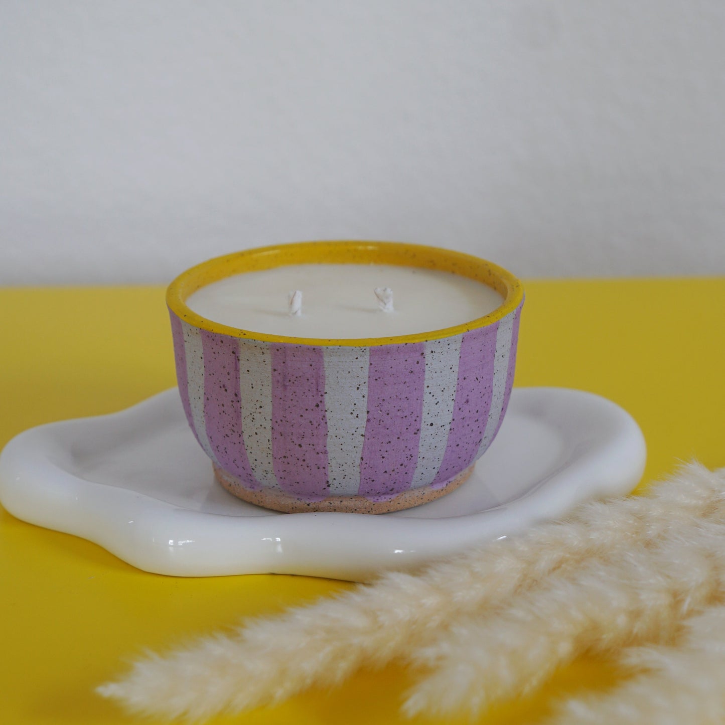 Striped candle in a decorative holder on a yellow surface with dried plants.