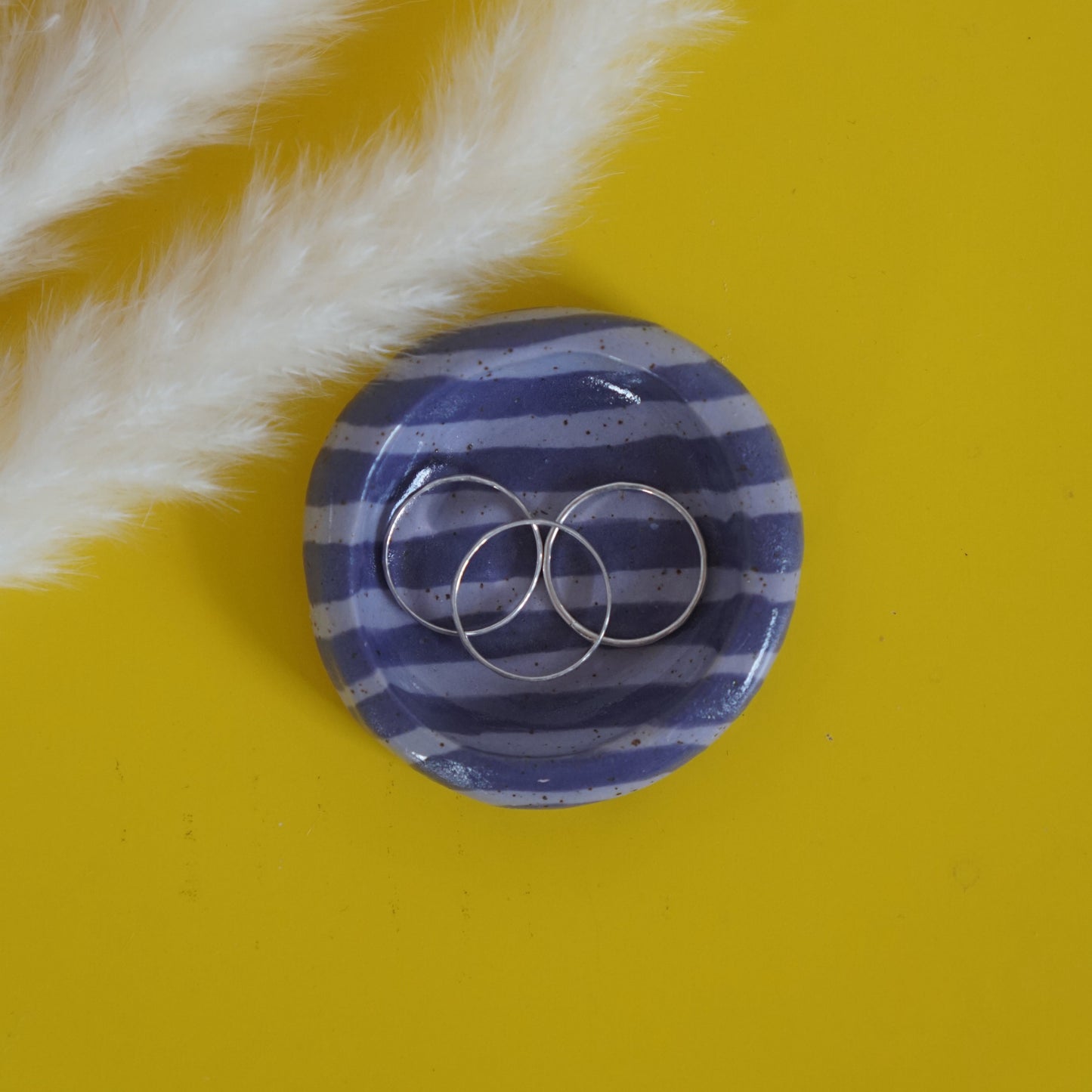 Purple striped ceramic ring dish with silver rings on a yellow background
