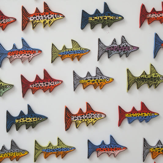 Colorful rainbow trout ceramic magnets arranged in a grid on a white background