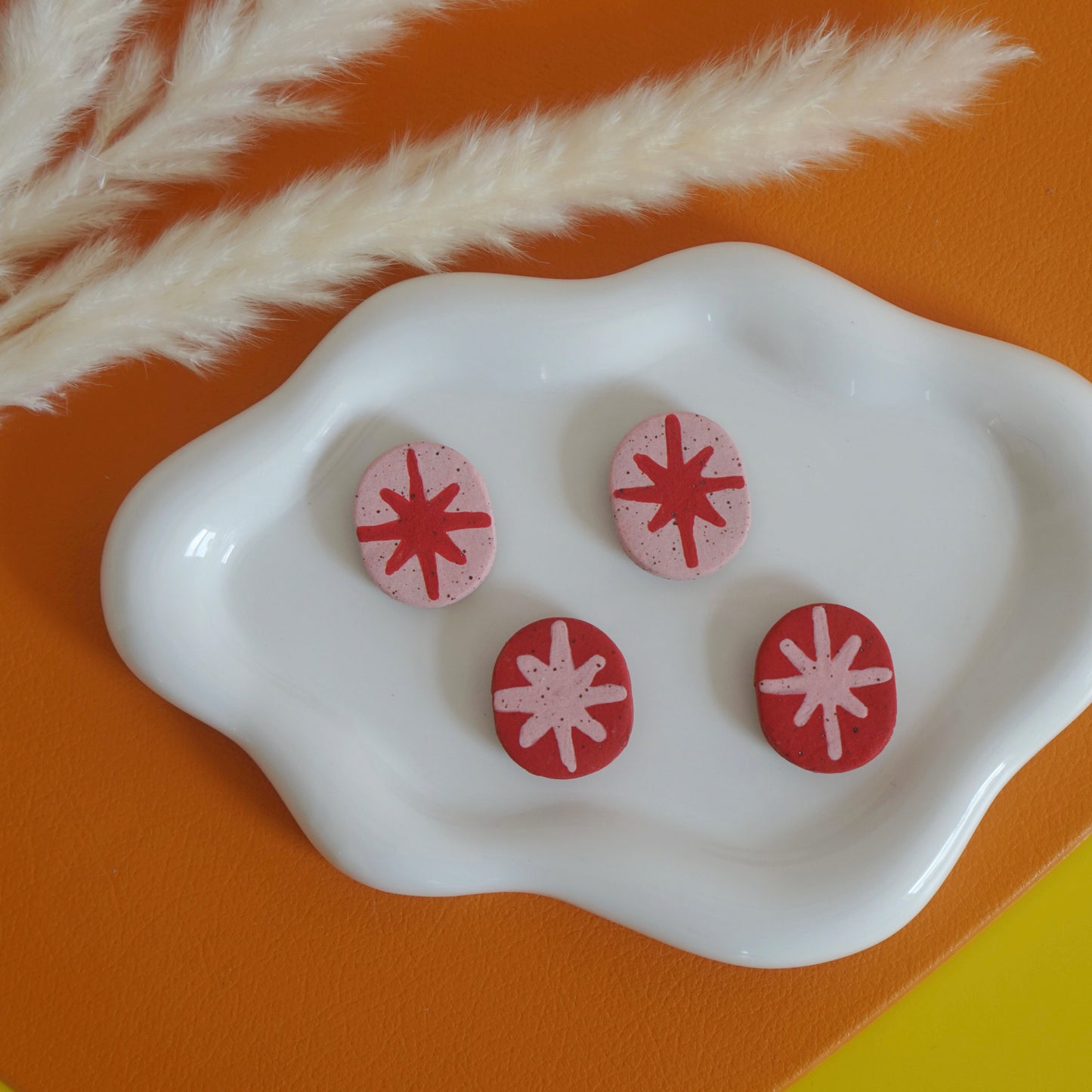 Red and Pink retro star ceramic magnets on a white dish with a natural branch on an orange and yellow background