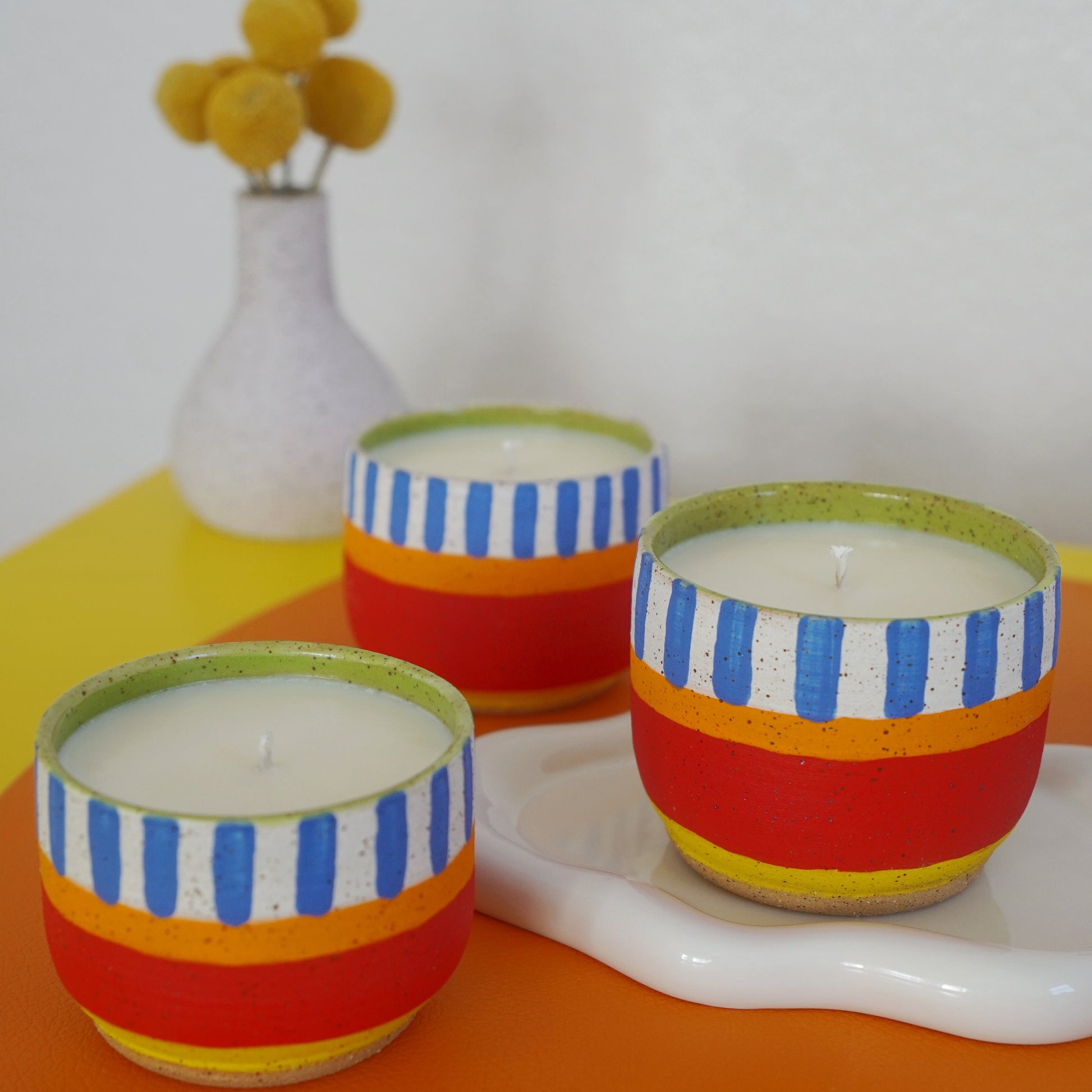 Three colorful striped candles on a white surface with a yellow background
