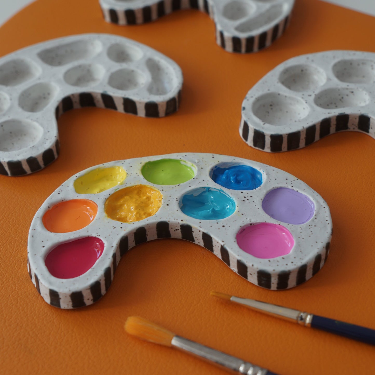 Ceramic Paint palette with a colorful palette and paintbrushes on an orange background