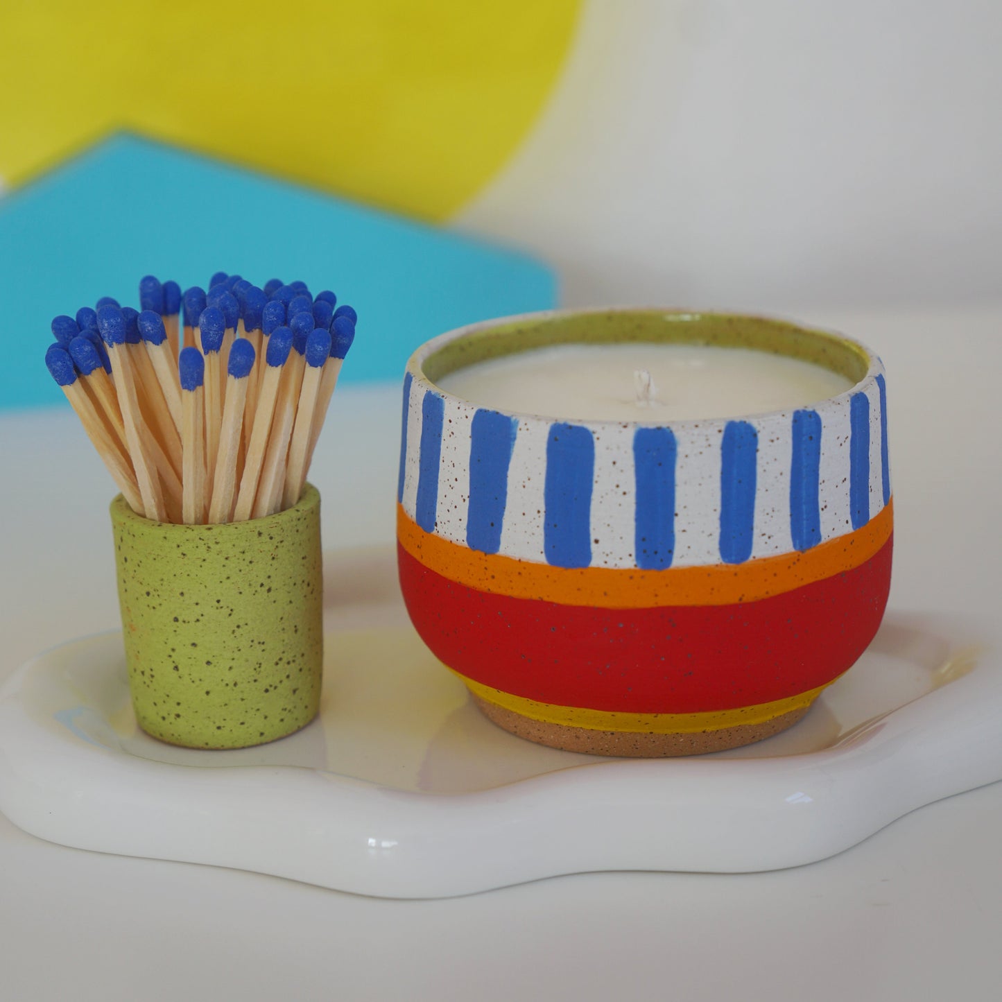 Colorful striped candle and green holder with matches on a white surface.
