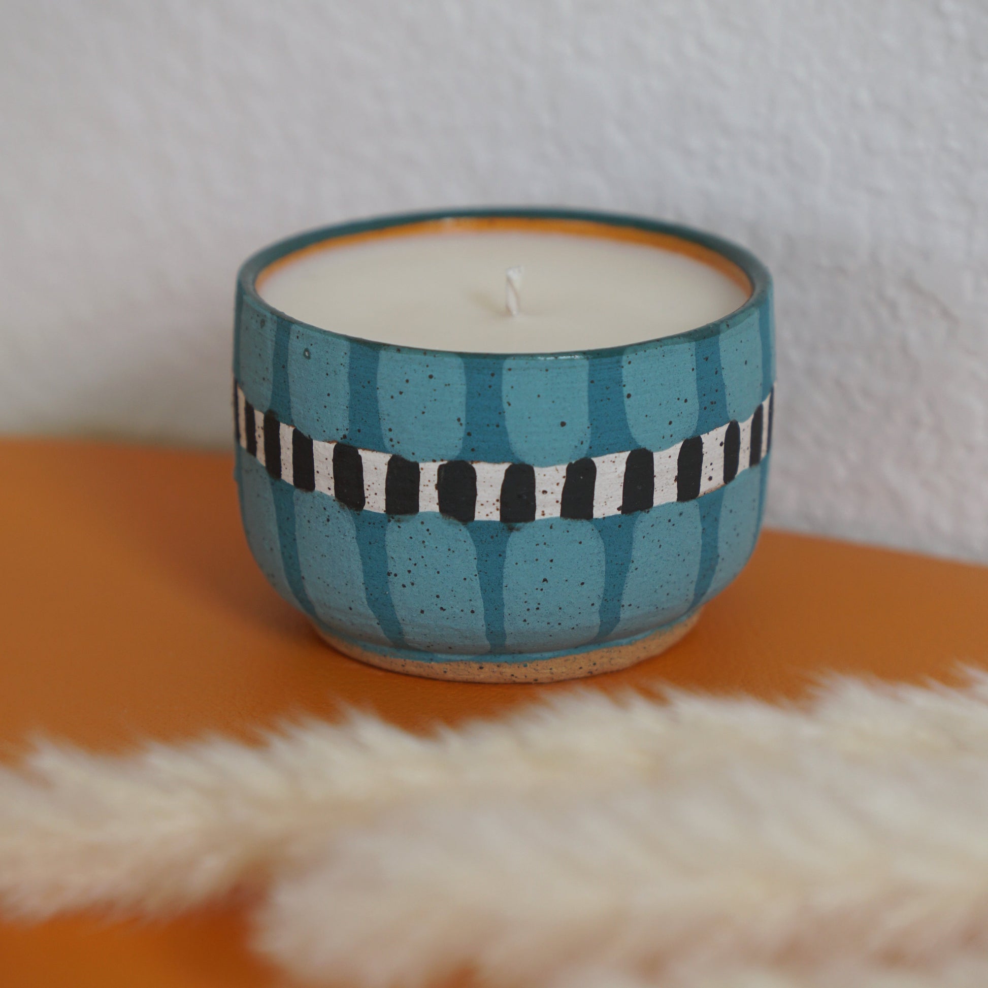 Ceramic candle holder with striped design on an orange surface