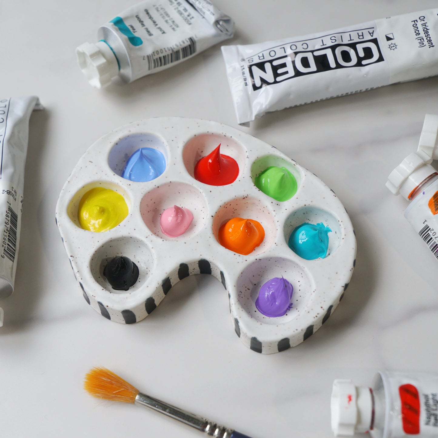 Artistic palette with colorful paint swatches, tubes of paint, and a brush on a white background