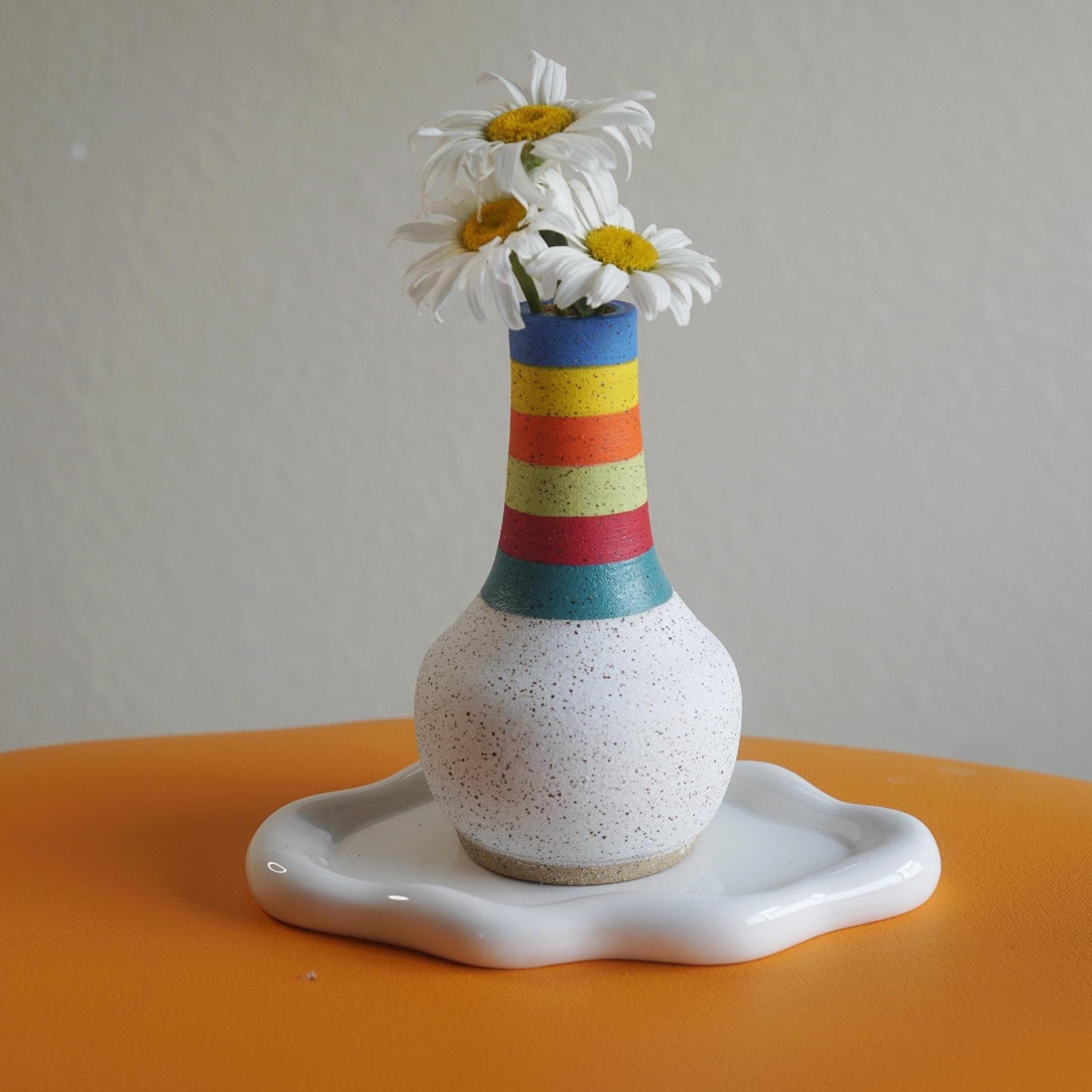 Colorful striped vase with flowers on a white plate against a gray background