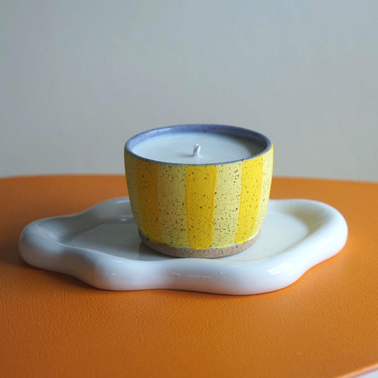 Ceramic candle holder with a yellow and blue striped design on an orange surface.